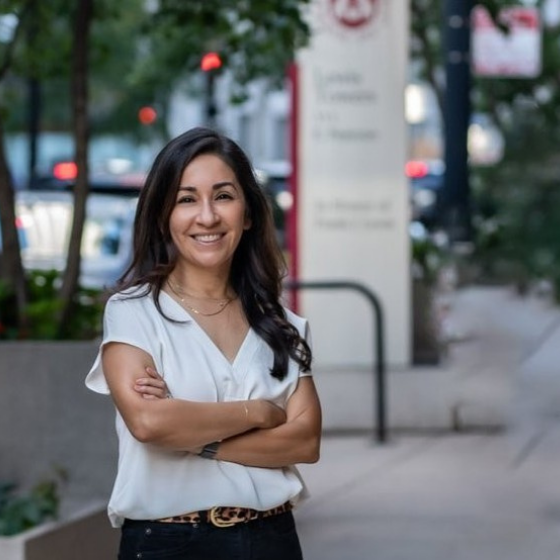 A woman smiling with long brown hair, wearing a white top and standing in front of a Loyola University Chicago Water Tower Campus building.